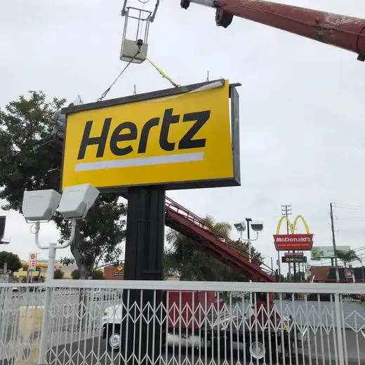 Crane installing a Hertz pole sign